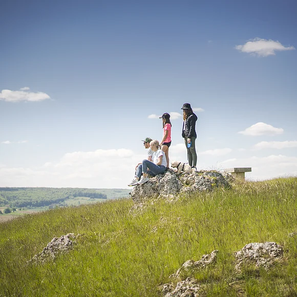 Familie mit Hund sitzen auf dem Bubenheimer Berg auf einem Felsen. Kinder stehen hinter den Eltern