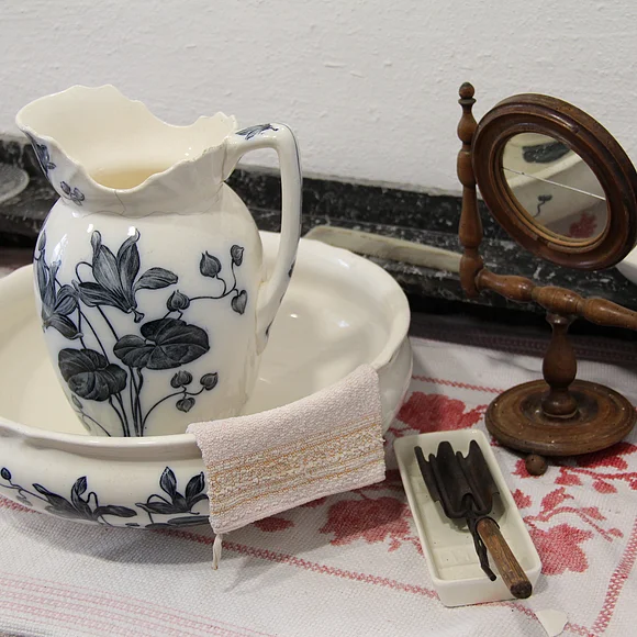 Ein Waschtisch mit weiß-blauer Waschschüssel, weiß-blauem Waschkrug und kleinem Spiegel