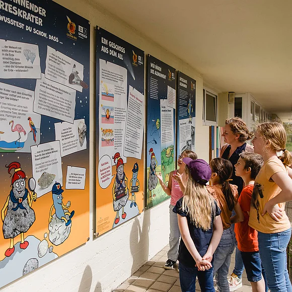 Eine Gruppe Kinder betrachtet Informationstafeln an einer Hauswand.