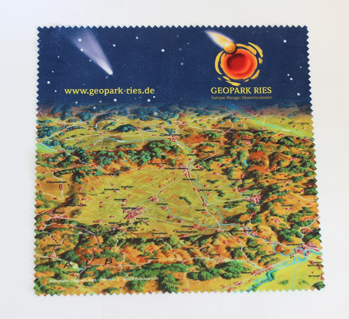 Auf einem Brillenputztuch ist eine Zeichnung des Rieskraters abgebildet, die nach oben hin in dunkelblauen Himmel mit Sternen und dem Logo des Geopark Ries übergeht.