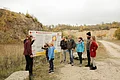 Eine Gruppe Personen mit Erwachsenen und Kindern steht vor einer Informationstafel in einem ehemaligen Steinbruch.