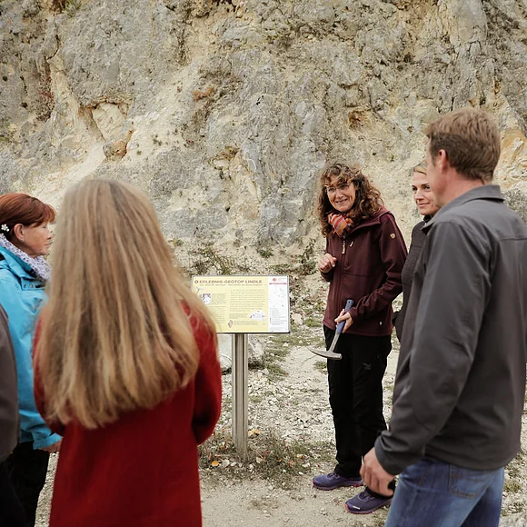 Eine Gruppe Personen steht um eine kleine Informationstafel, die sich vor einer Felswand befindet.