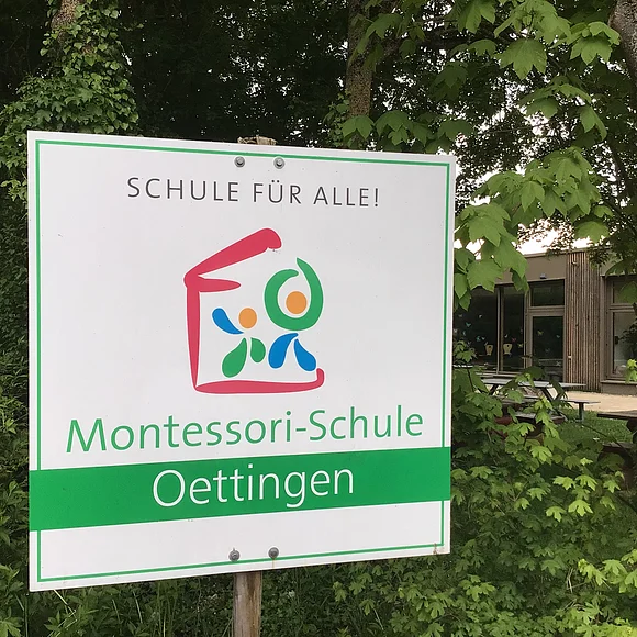 Montessori-Schule Oettingen Das Bild zeigt ein Schild mit dem Text "Schule für Alle - Montessori-Schule Oettingen"