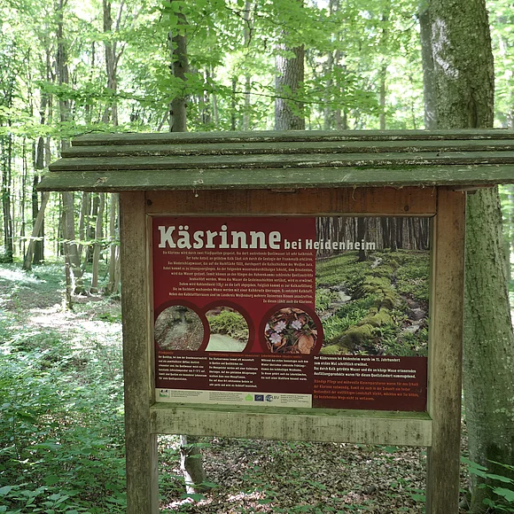 In einem Wald steht eine holzüberdachte Informationstafel mit dem Titel "Käsrinne bei Heidenheim".