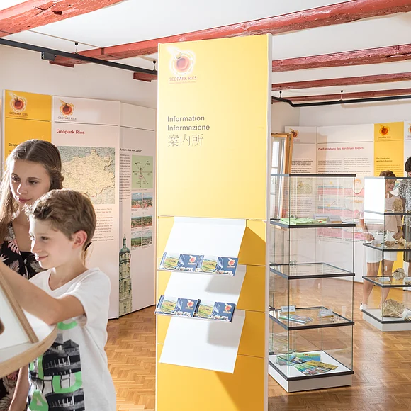 Eine Familie befindet sich in einem Ausstellungsraum mit Glasvitrinen und Informationstafeln.