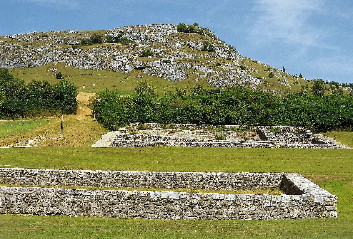 Am Fuße eines felsigen Hügels befinden sich die Grundmauern von ehemaligen Gebäuden.