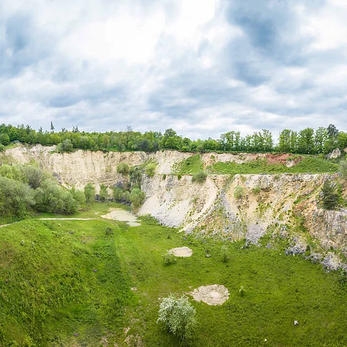 Blick in einen großen ehemaligen Steinbruch mit Büschen und Bäumen.