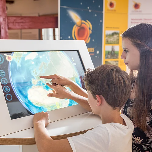 Zwei Kinder bedienen auf einem Monitor die Anwendung "Uhr der Erdgeschichte".