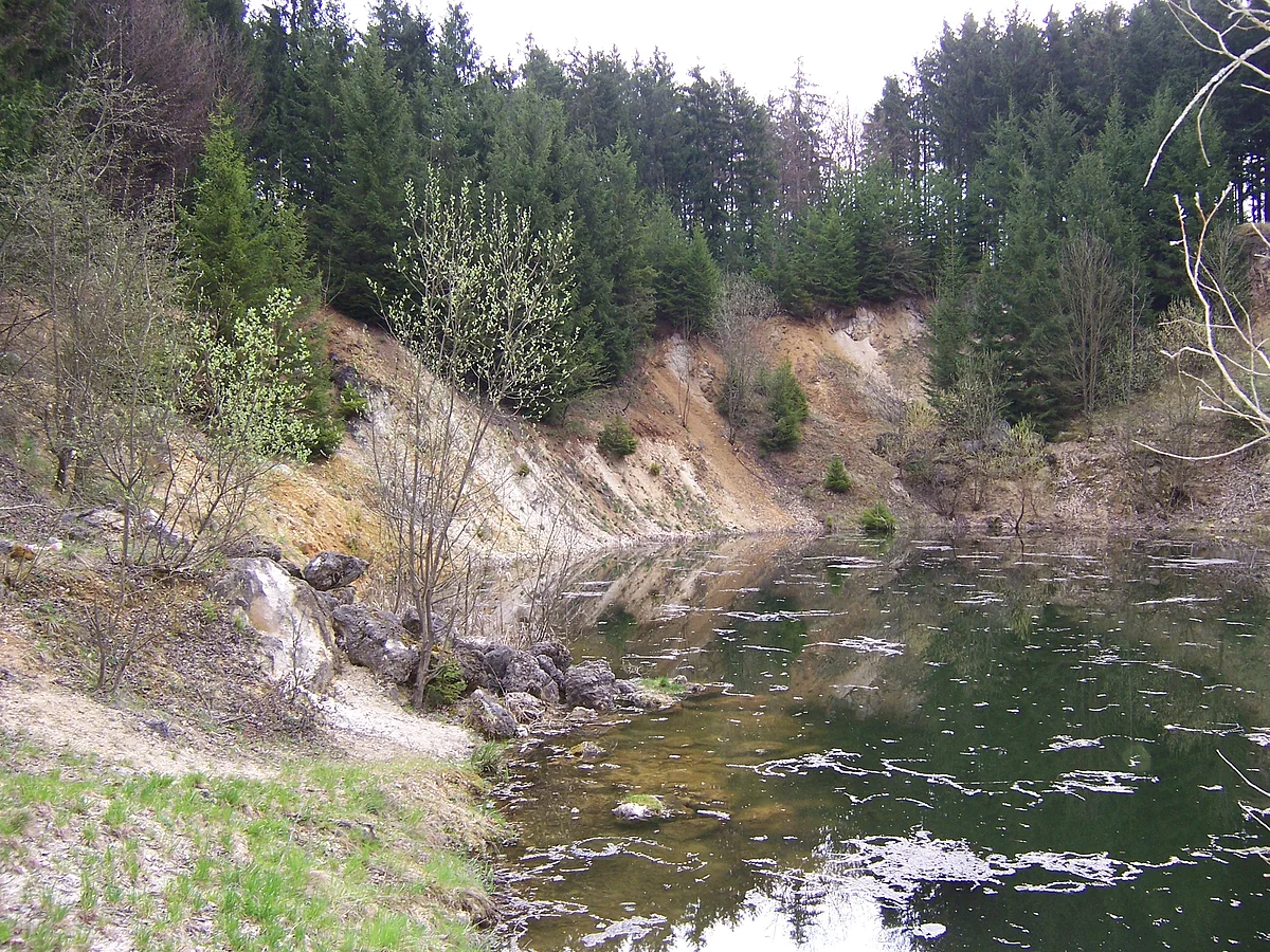 Steile Hänge mit Wald und teilweise offenem Boden umgeben einen See.