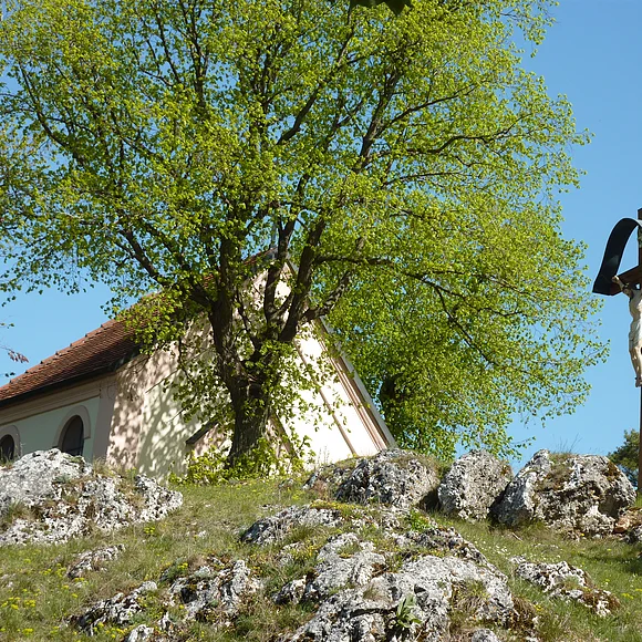 Am Fuße einer Kapelle ragen einige Felsblöcke aus der Wiese.