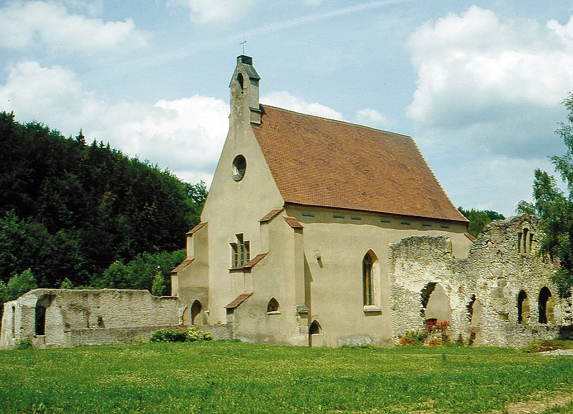Monastero certosino di Christgarten An eine kleine braune Kirche schließen sich teils verfallene Mauern mit Rundbögen an.
