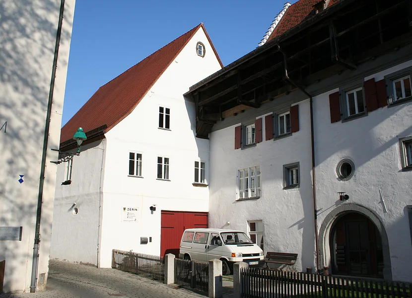 Lo ZERIN di Nördlingen Neben dem Tor eines Hauses mit weißer Fassade hängt ein Schild mit der Aufschrift "ZERIN". Es ist unmittelbar an ein anderes Haus angebaut.