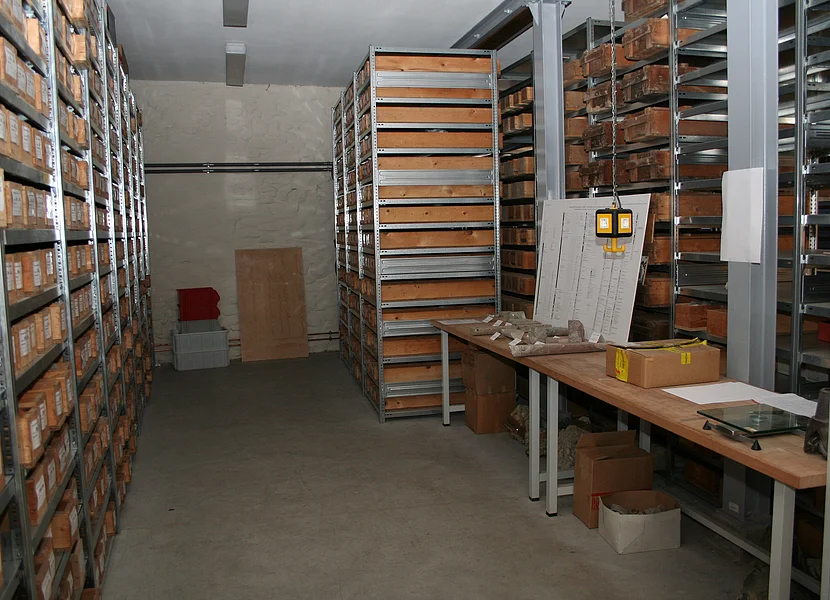 L’archivio dei campioni carotati In einem Raum stehen mehrere Metallregale mit Holzkästen, die beschriftete Bohrkerne enthalten.