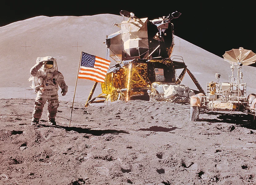 L’allunaggio della missione Apollo Ein Astronaut steht neben einer USA-Flagge auf der Mondoberfläche. Im Hintergrund sind zwei Mondrover zu sehen.