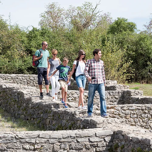 Lauschtour Rieskrater-Tour Fünf Personen laufen über die gemauerten Fundamente eines ehemaligen Gebäudes. Im Hintergrund ist eine Buschreihe zu sehen.
