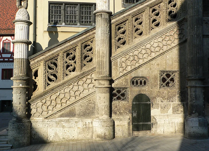 Scalinata esterna del Municipio di Nördlingen Die Freitreppe vor einem Gebäude ist aus dem Gestein Suevit gefertigt. Unterhalb des Geländers befinden sich kunstvolle Verzierungen.