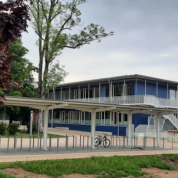 Seitenansicht der Rückseite der Oettinger Grund- und Mittelschule. Im Vordergrund der überdachte Fahrradständer mit einem Fahrrad.