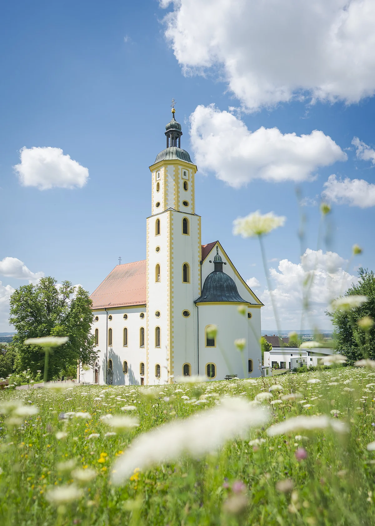 Wallfahrtsbasilika Maria Brünnlein, Wemding Kirche mit Turm und rotem Dach auf einer Wiese, blauer Himmel mit Wolken im Hintergrund.