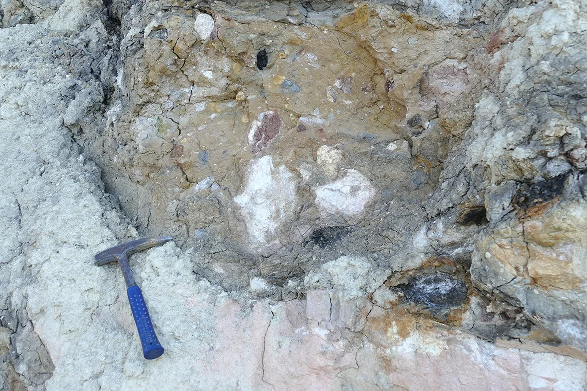 Bunte Breccie mit daneben liegendem Geologenhammer