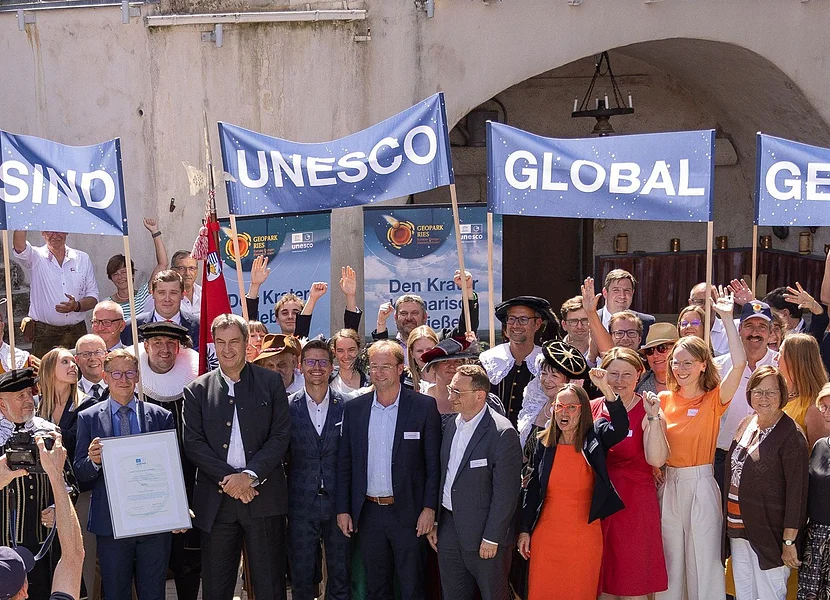 Eine große Gruppe Personen hält Banner mit der Aufschrift "Wir sind UNESCO Global Geopark" in die Höhe.